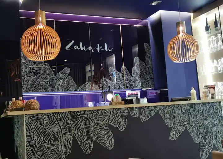 Bar Restauracji Zakątek z granatową ścianą, logo i wiklinowymi lampami nad ladą we wzór liści