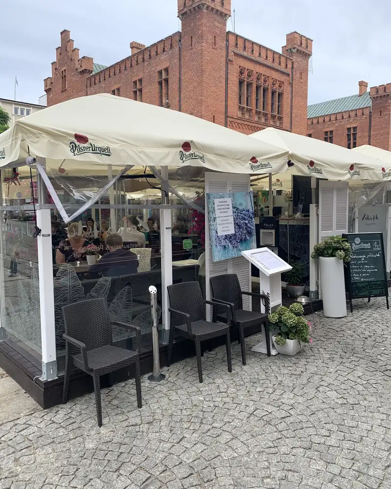 Ogródek restauracji pod białymi parasolami, w tle ceglany ratusz w Kołobrzegu